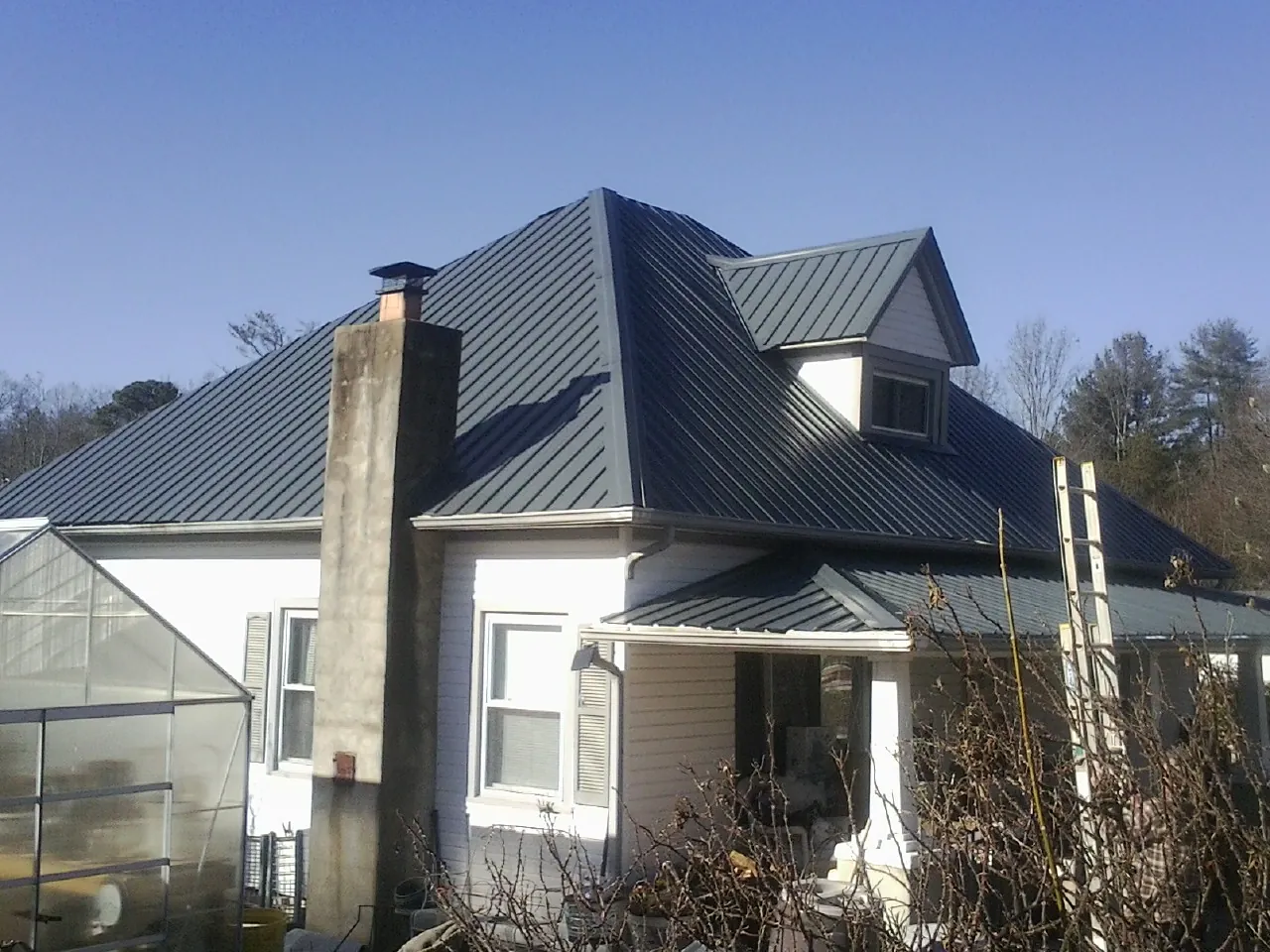 Dark blue standing seam metal roof on a white farmhouse with dormer — Slate & Tile Roof Repair by Roofing Brothers in Redfield