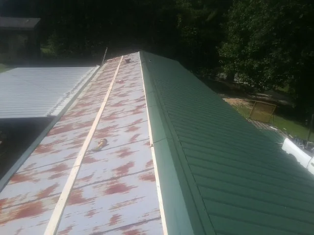 Old rusted panels beside newly installed green metal roofing — Wind Damage Roof Repair by Roofing Brothers in Redfield