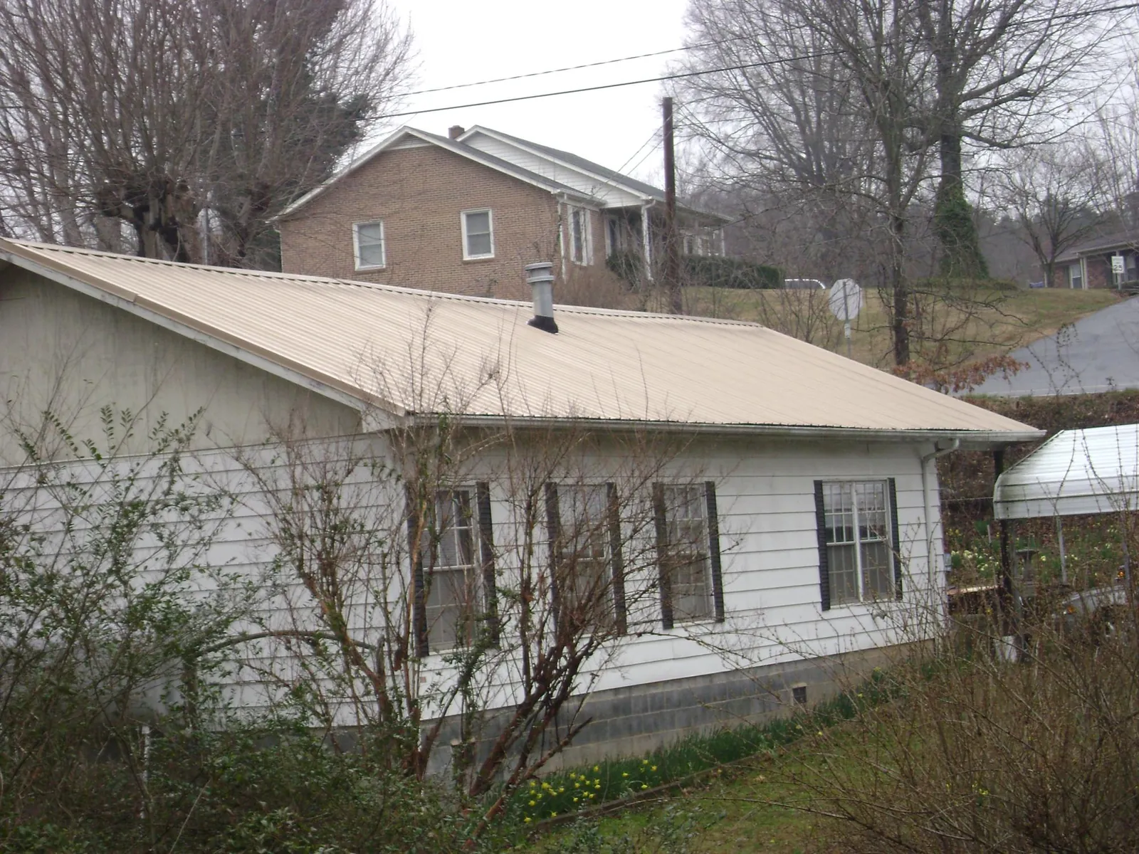 Tan metal roof on a white sided house set into a hillside — Commercial Roofing by Roofing Brothers in Redfield